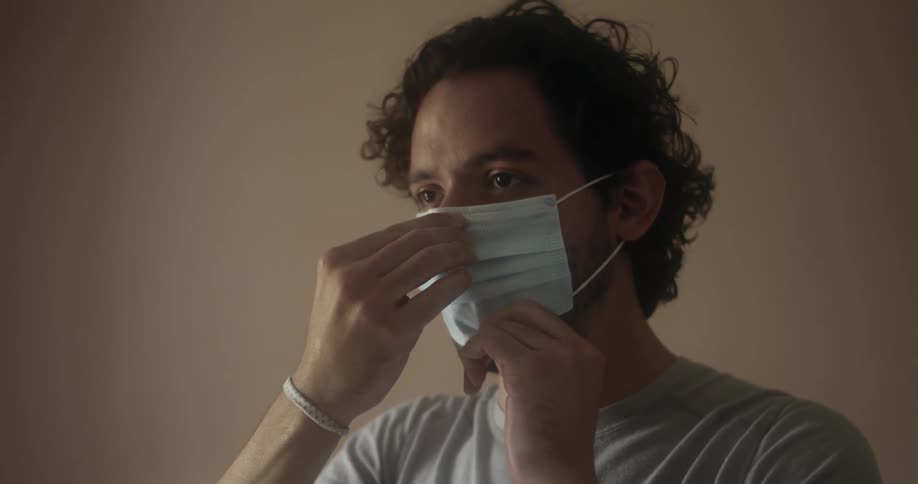 A man putting on and adjusting a blue face mask