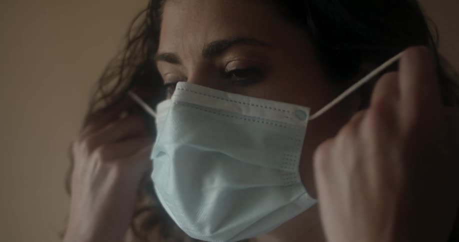 A woman wearing a disposable mask over her nose and mouth removes it