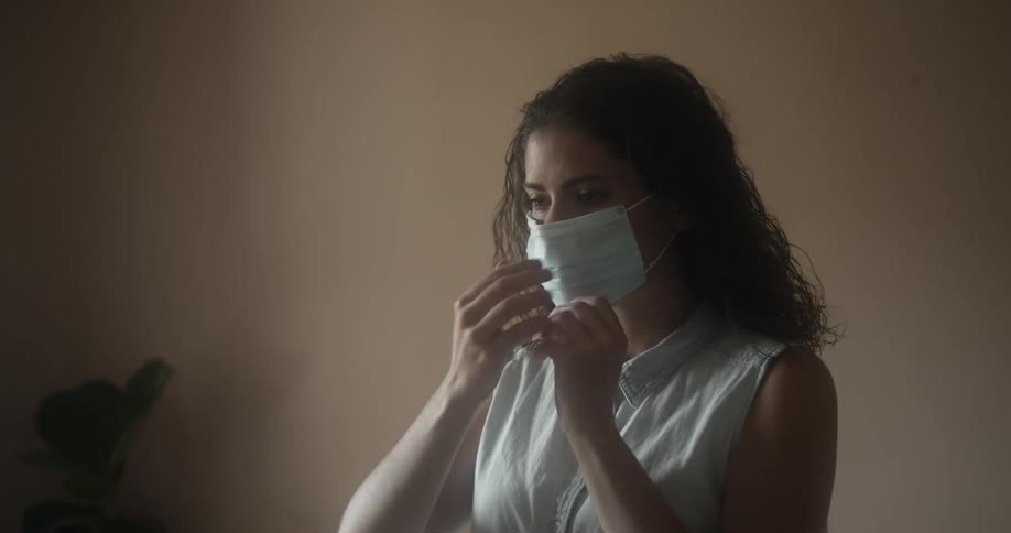 Woman standing in room puts on face mask