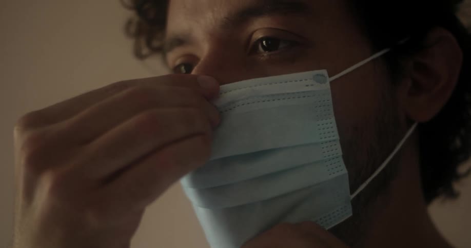 A bearded man putting on a medical face mask