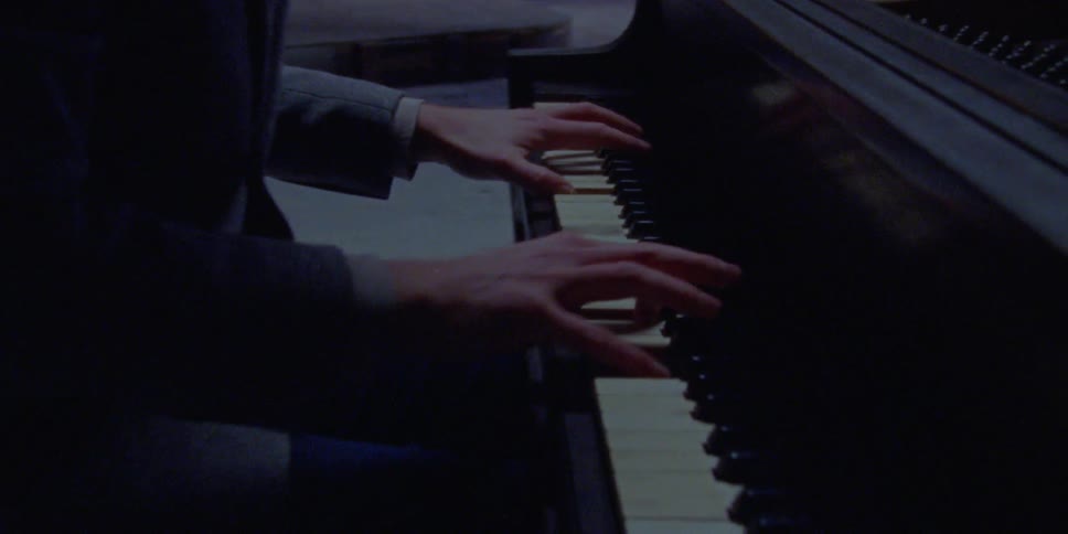 A young man in a suit playing a piano in a dim room