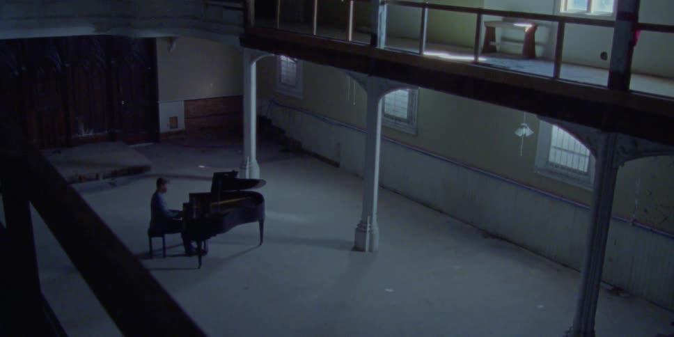 A man plays the piano in a large empty room