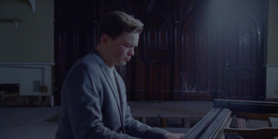 A young man playing a piano in a small empty auditorium