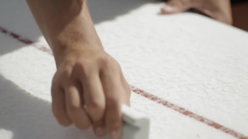 A man smooths the bottom of a surfboard