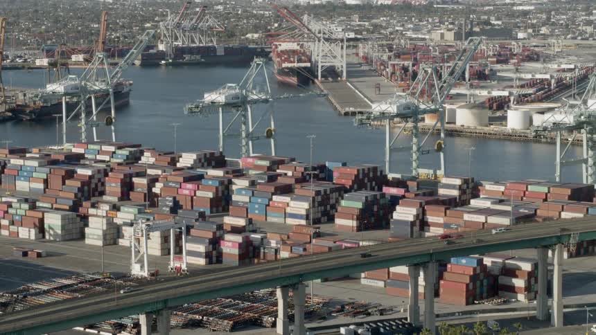 Shipping containers stacked high in a shipping yard next to a freeway bridge
