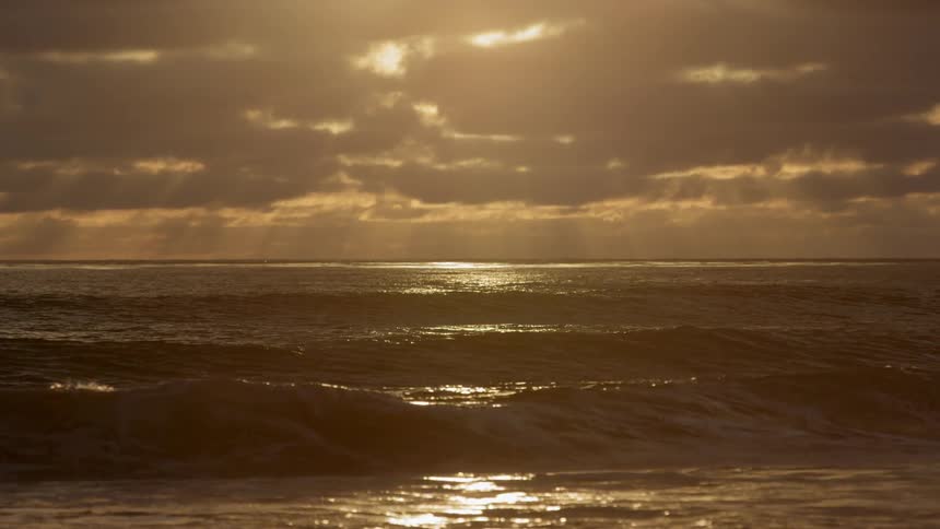 Waves roll under a cloudy sky at sunset