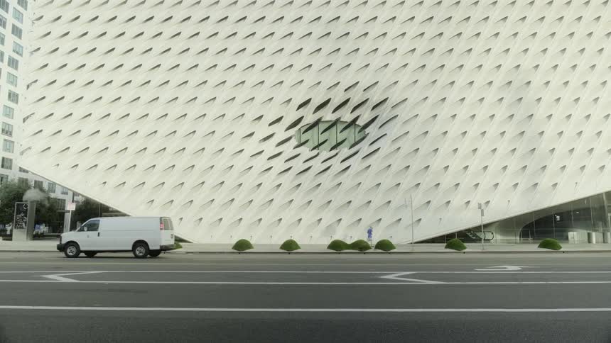 Vehicles pass by a pedestrian and a large unique city building
