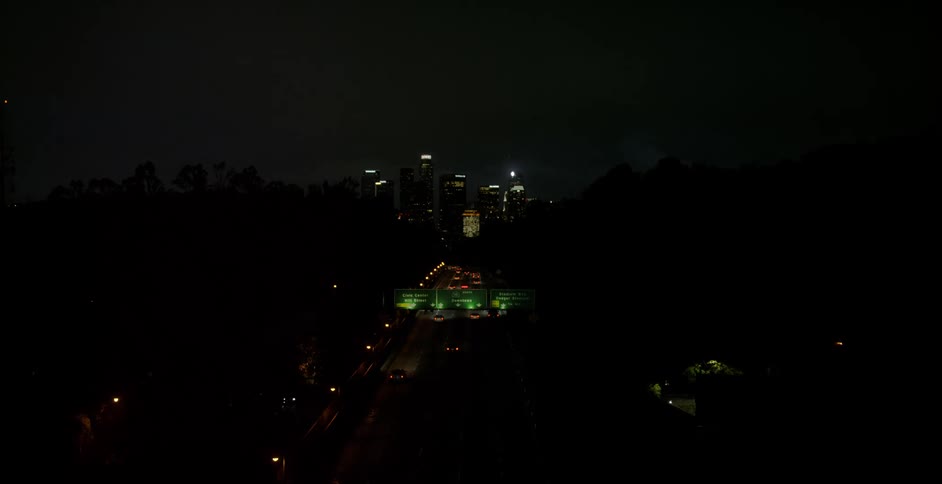 Vehicles drive on a highway into a city at night