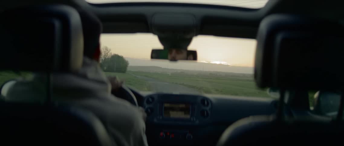 A man drives down a rural two lane road at sunrise