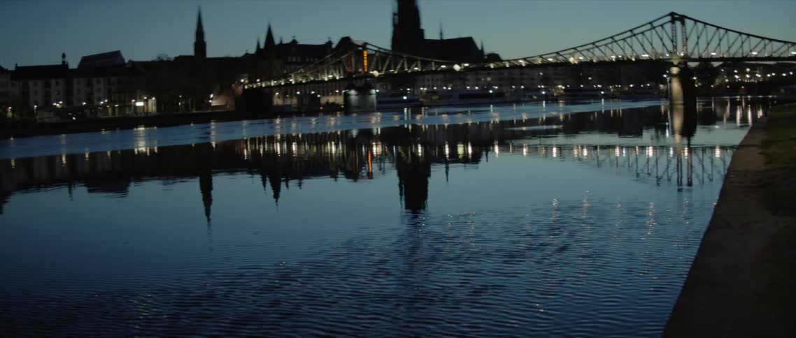 The lights from a bridge and city are reflected on the surface of the river at night