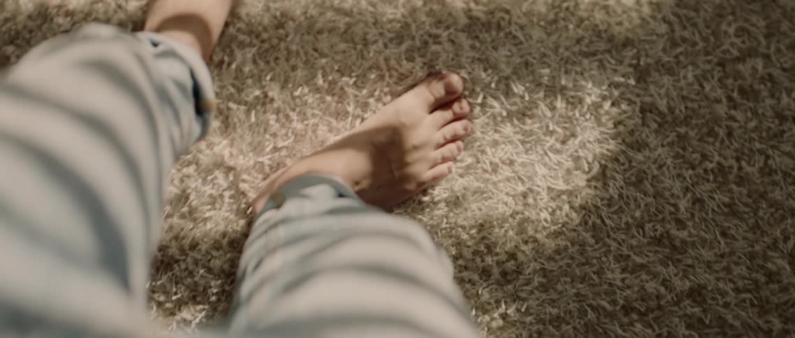 A person rubs their bare feet on the thick pile of a shaggy rug with sunlight and shadows