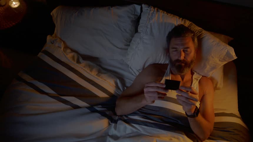 A man is laying in bed and looking at a photograph