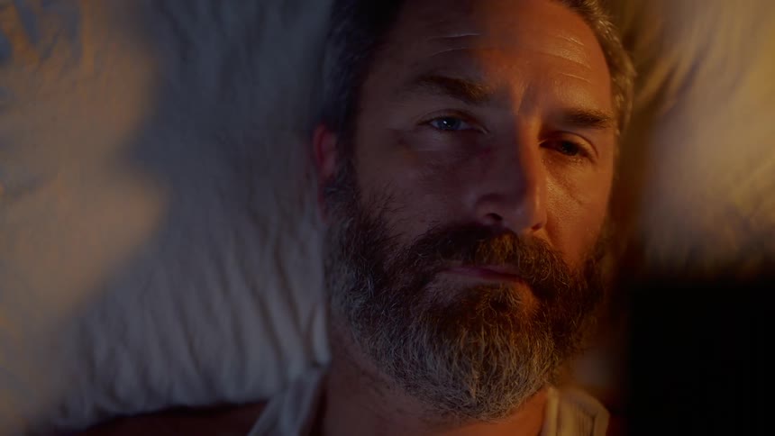 Man lying down on the bed looks at the photograph in the bedroom