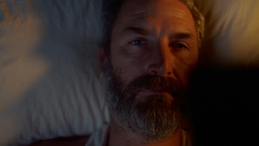 Bearded man lying on the bed looks at the photograph and is filled with nostalgia in the bedroom