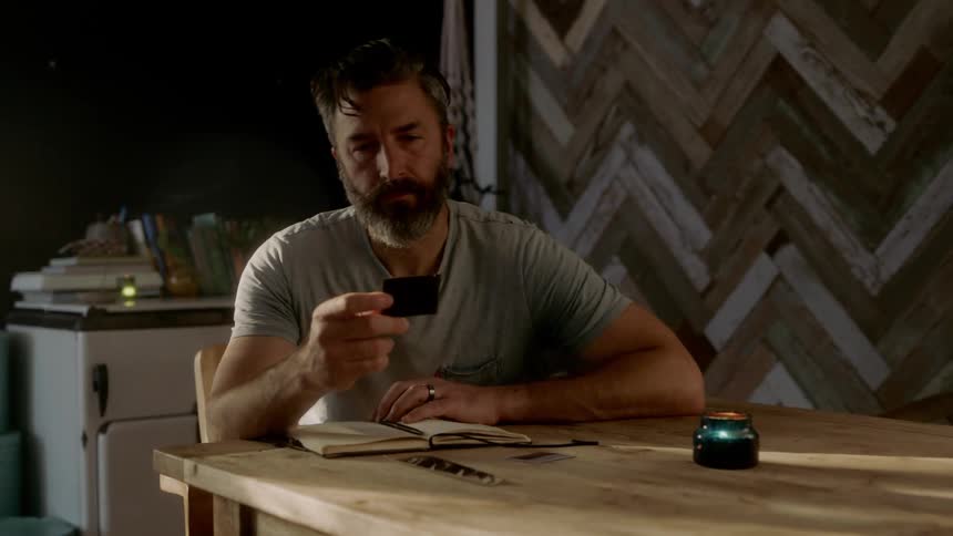 A man writes in a notebook at a kitchen table