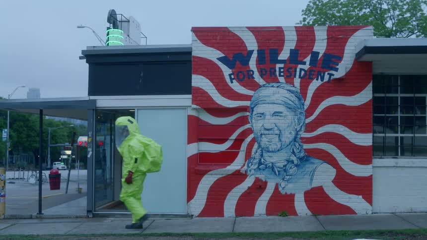 A person with a hazmat suit standing in front of a building with a mural then walking away