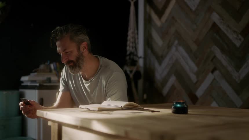 Bearded man sitting at the table looks at a photograph and smiles