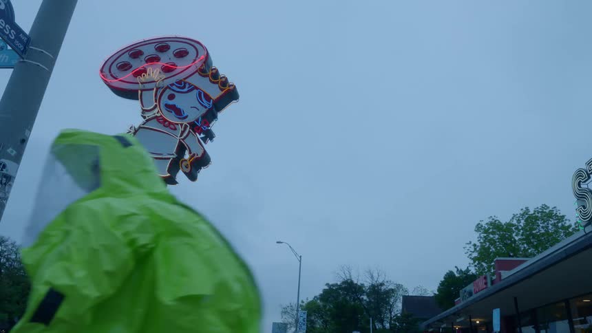 A man in a fluorescent safety suit walks past a pizza restaurant