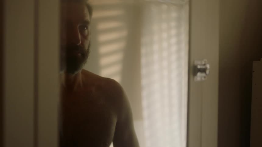 A man standing shirtless before a mirror looking at his reflection