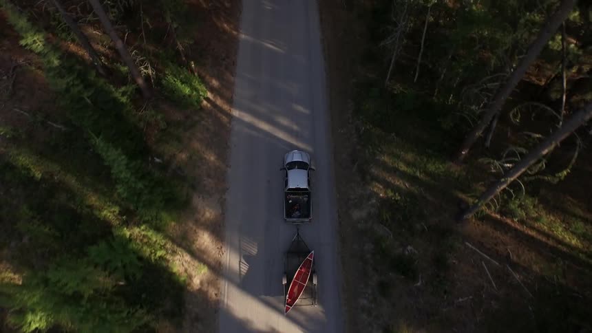A truck hauling a kayak rides down a forest road