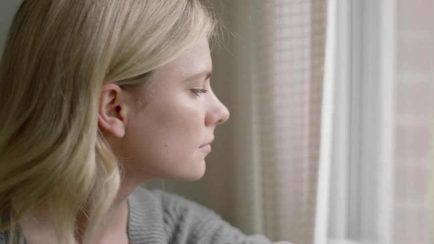 Blonde woman sitting near window looking out below