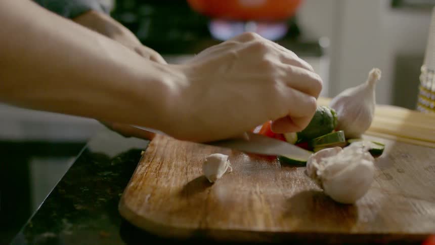 Person crushes garlic on chopping board with knife near gas stove