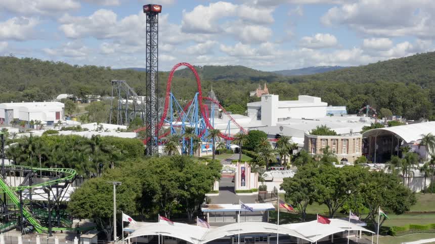 The empty parking lot and still rides of an amusement park with hills and trees behind on a sunny day