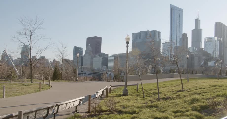 The empty benches and walkways of a park with the city skyline behind on a bright sunny day