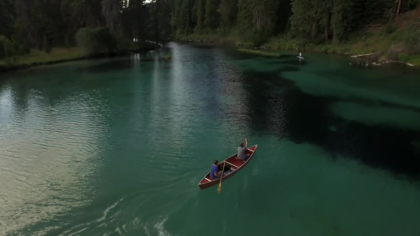 Two men paddle a canoe along a river in the woods