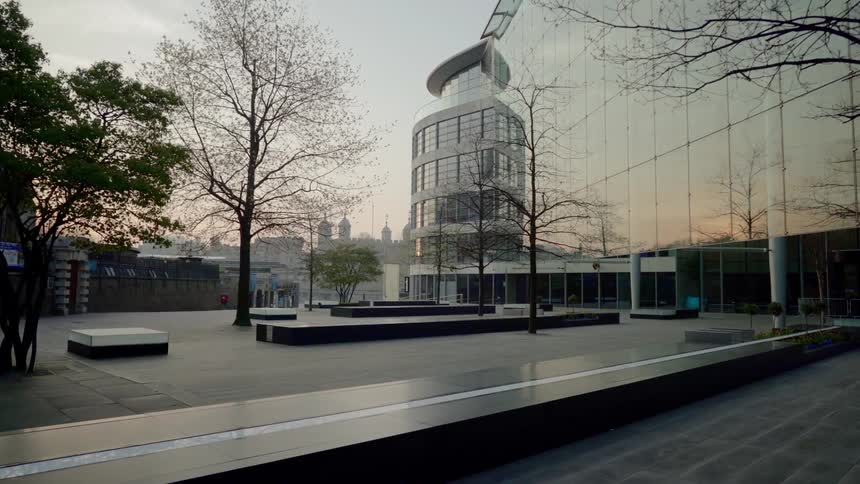 The sunset sky and trees in a plaza are reflected in a buildings glass facade