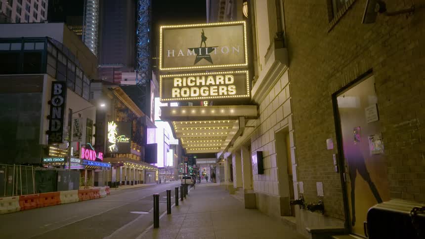 Car drives along empty street past businesses with electric signs near skyscrapers at night