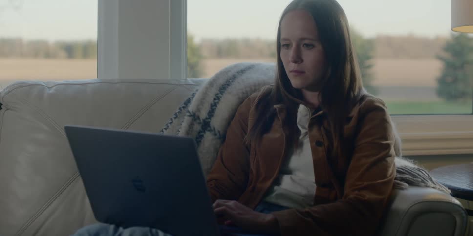A woman works on a laptop while sitting on a couch