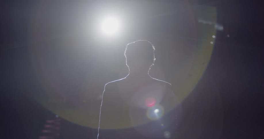 A spotlight shines on a man on stage before an empty auditorium