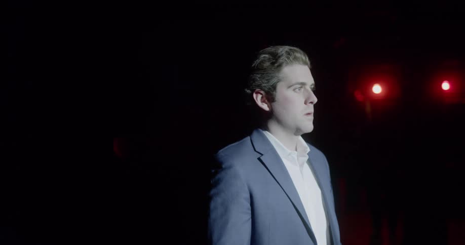 A man stands in front of a spot light on a stage