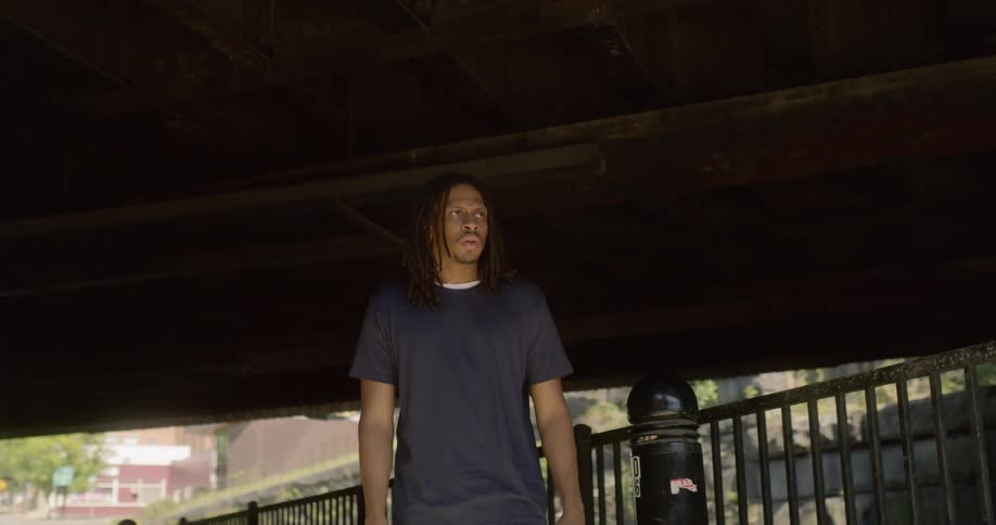 A man stands under a bridge as stares into the distance