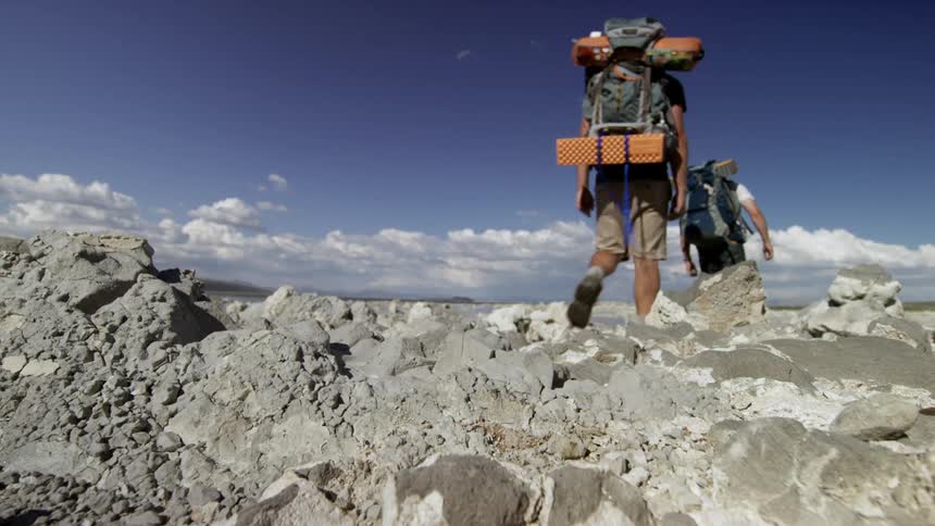 Two men wearing backpacks hike on a rocky trail