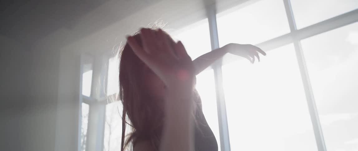 A woman in black dances in front of a window