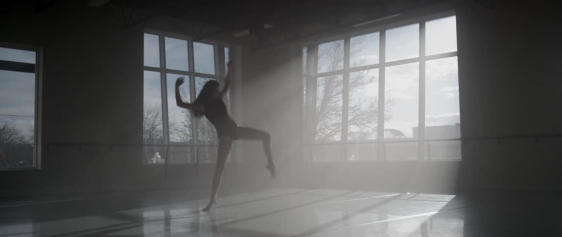 A woman dances in front of windows in a studio