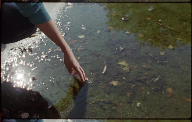 A person crouches by a puddle and dips their hand in the water