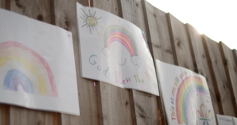 A wooden fence with papers of childrens drawings on it
