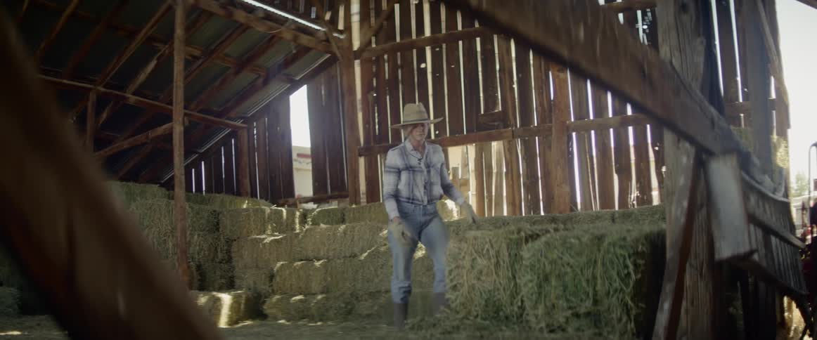 Blonde woman carries a bale of hay in the barn