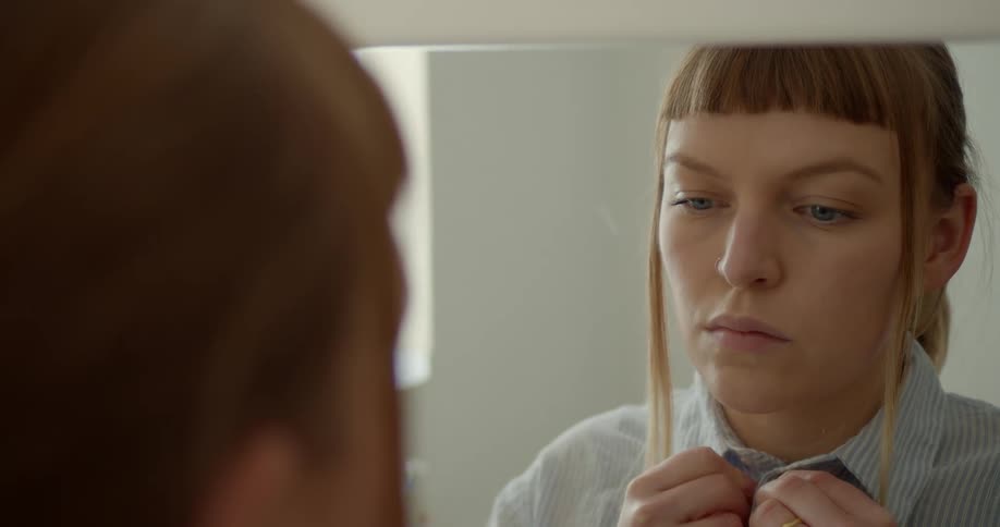 Sad woman standing in front of mirror buttoning her shirt