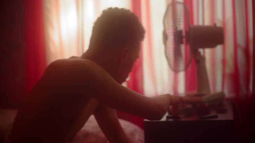 A man sits on his bed swaying to music then picks up a marijuana cigarette and lights it