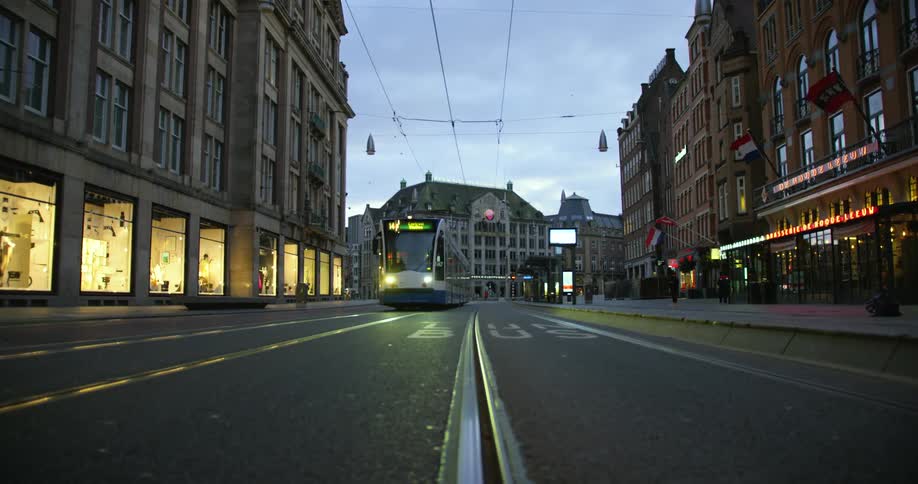 A train drives down a city street as pedestrians walk along