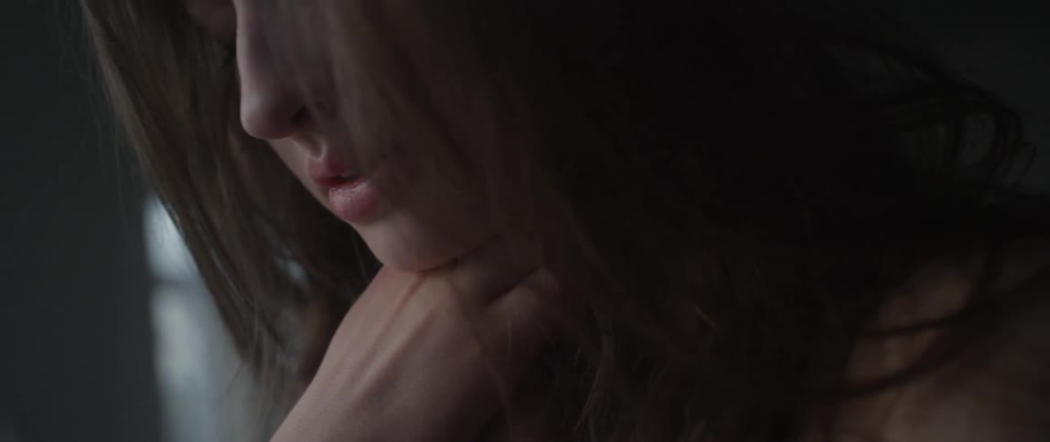 A woman puts her hand to her chin by a window