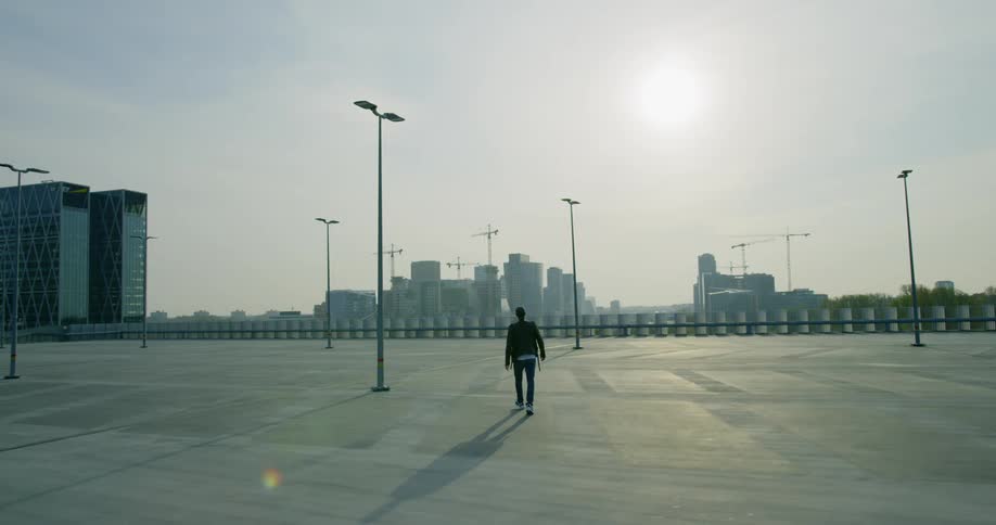 A man walking in an empty parking lot with buildings in the distance