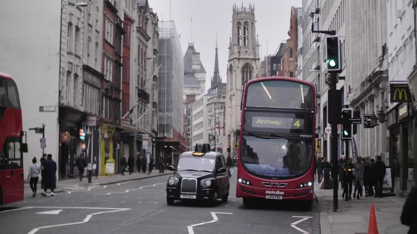 A london bus and taxi drive as the traffic lights turn green