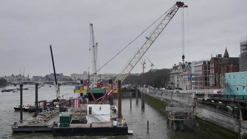 Cranes line a riverfront next to a city