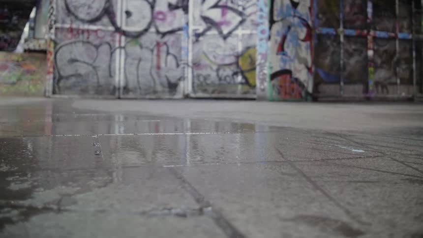A roller skater skating pass a wall covered in graffiti on a rainy day