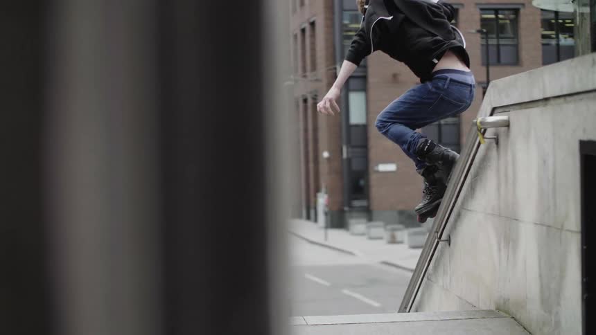 A boy with inline skates skating down a concrete handrail